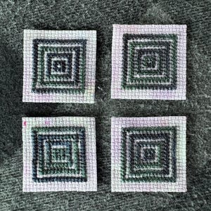 May include: Four square cross-stitch pieces featuring a concentric square pattern in shades of dark green and black. Each piece is worked on a light, mottled lavender fabric base, creating a geometric design with a visible grid texture throughout.