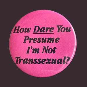May include: A round, bright pink button with black text. The text reads: "How Dare You Presume I'm Not Transsexual?" The button has a glossy finish and is set against a dark background.