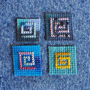 May include: Four square needlepoint patches featuring embroidered spiral patterns. The top left patch is blue and grey, the top right is dark blue with pink, the bottom left is bright blue with pink, and the bottom right is teal with yellow.