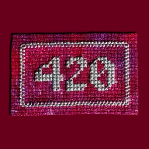 May include: A rectangular patch featuring a cross-stitched design on a variegated magenta and purple fabric. The number 420 is embroidered in white thread in the center, surrounded by a white stitched rectangular border frame.