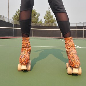 Könnte beinhalten: Eine Person trägt schwarze Leggings mit transparenten Einsätzen und orangefarbene und braune Rollschuhe mit beigen Rädern. Die Rollschuhe haben ein Schlangenhautmuster. Der Hintergrund ist ein grüner Tennisplatz.