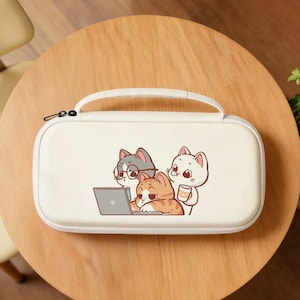 May include: A cream-colored carrying case with a black zipper and a white handle. The case features a cartoon illustration of three cats: one with glasses using a laptop, another holding a coffee cup, and a third looking on.