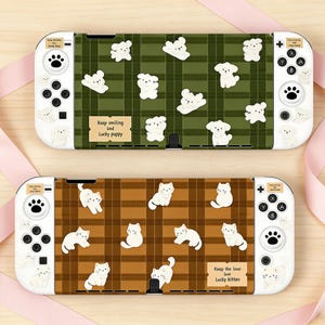 Puede incluir: Dos fundas para consola Nintendo Switch. Una presenta un patrón de cuadros verdes con ilustraciones de cachorros blancos y el texto "Keep smiling and Lucky puppy". La otra tiene un patrón de cuadros marrones con ilustraciones de gatos blancos y el texto "Keep the love love Lucky kitten."
