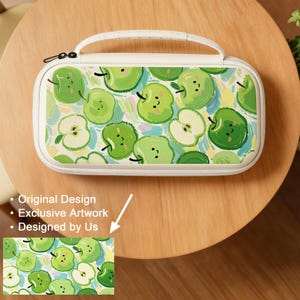 May include: A white carrying case with a handle, featuring a pattern of green apples with smiling faces. The case has a zipper closure and a white border. The design includes a small image of the apple pattern.