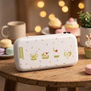 以下が含まれることがあります： 白い長方形のケースで、ジッパー付き。カラフルな振りかけとデザートをテーマにしたイラストで装飾されています。ケースには「DESSERT」の文字が入った緑色の長方形があります。イラストには、ウサギの入ったティーカップ、ケーキのスライス、カップケーキが含まれています。