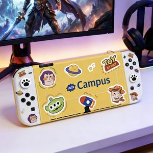 May include: Yellow Nintendo Switch case with Toy Story character stickers. The case has the word "Campus" printed on it. The left side has a paw print button and the right side has a Toy Story logo.