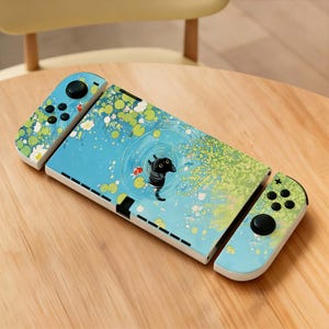May include: A blue and white Nintendo Switch console with a custom design featuring a black creature in a pond with lily pads and koi fish. The controllers have a matching design with black buttons.