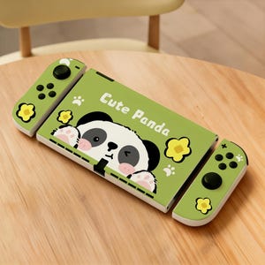 May include: A green and white Nintendo Switch case with a panda design. The case features the text "Cute Panda" and includes two green controllers with black buttons and yellow flower accents. The panda has black and white fur and pink paws.