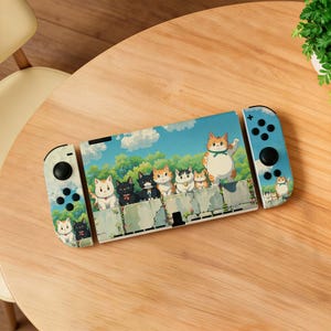 May include: A Nintendo Switch console with a custom skin featuring an illustration of several cartoon cats on a wall, set against a blue sky and green foliage background. The Joy-Con controllers are light blue.