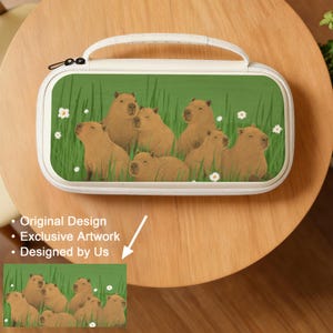 Puede incluir: Un estuche blanco con asa, con un fondo verde con ilustraciones de carpinchos y flores blancas. El estuche tiene una cremallera negra y un asa blanca. También se ve el texto "Original Design", "Exclusive Artwork" y "Designed by Us".