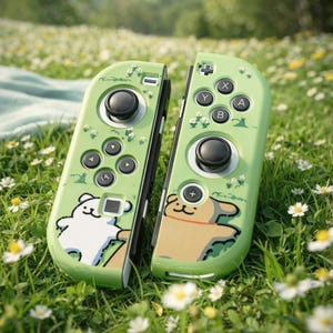 Op de afbeelding: Twee groene gamecontrollers met zwarte knoppen en een cartoon hond en beer ontwerp. De controllers zijn versierd met kleine witte bloemen. De controllers liggen op een bed van groen gras en witte bloemen.