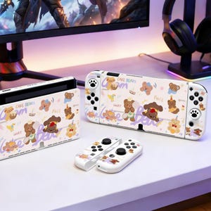 Puede incluir: Consola y mandos Nintendo Switch blancos con un patrón repetido de osos de dibujos animados, pasteles y texto. El texto incluye las palabras "Cake Bears", "Lucky" y "Fall". La consola y los mandos están sobre una superficie blanca.