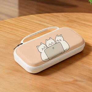 May include: A rectangular, peach-colored case with a white zipper and handle. The case features a cartoon illustration of three white cats looking at a laptop with a heart symbol. The case is designed for electronics.