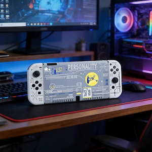 Puede incluir: Una consola Nintendo Switch gris y blanca con un diseño personalizado. El diseño incluye la palabra "PERSONALITY", un círculo amarillo con un gráfico de mando y varios elementos gráficos. La consola está sobre un escritorio con un ordenador y accesorios de juego.