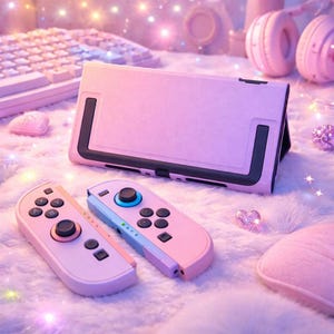 May include: A pink gaming console case and two matching controllers are displayed on a fluffy white surface. The case is rectangular with black accents, and the controllers have pink and blue color schemes. The scene is bathed in soft, ambient lighting.