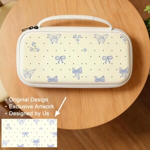 May include: Cream-colored carrying case with a handle, adorned with a pattern of light blue butterflies, bows, and small floral accents. The case has a black zipper and is set against a wooden table. The text on the image says "Original Design", "Exclusive Artwork", and "Designed by Us".