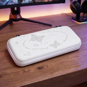 May include: A white carrying case with a zipper closure, featuring butterfly and floral designs. The case has the text "Dancing like butter in the dazzling summer". The case is on a wooden surface.