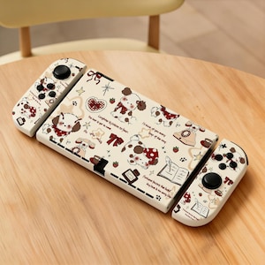 May include: A white gaming console and two detachable controllers featuring a repeating pattern of cartoon puppies, red bows, vintage telephones, and open books. The surface includes printed text phrases such as Laughter is poison to fear and Fortune favors the bold.