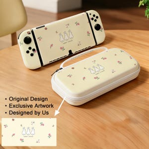 May include: A cream-colored Nintendo Switch console and carrying case, both adorned with a repeating pattern of small pink flowers and three cartoon rabbits. The case has a white zipper and handle.