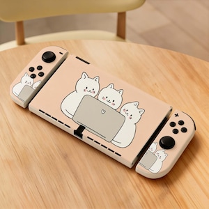 May include: A pink Nintendo Switch console with a playful cat design. The console features a light pink cover with three white cartoon cats gathered around a laptop. The controllers also have cat graphics.