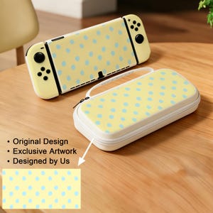 May include: A handheld video game console and a matching rectangular carrying case, both featuring a pale yellow background with a light blue polka dot pattern. The console has black buttons and joysticks. Text reads: Original Design, Exclusive Artwork, Designed by Us.