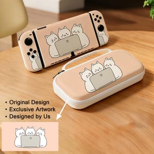 May include: A pink Switch console and carrying case featuring a cartoon design of three white cats looking at a laptop. The case has a white zipper and handle. The console has black buttons and joysticks.
