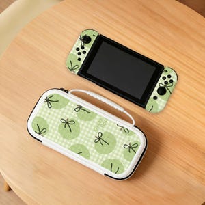 May include: A green Nintendo Switch console and a matching carrying case. The console and case have a light green apple pattern with the text "Green Apple" on the case. The case has a white handle and zip.