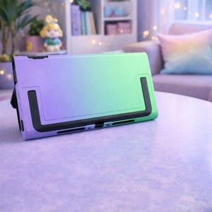 May include: A gradient purple to green protective case for a handheld gaming device. The case has black accents and a built-in stand. The device is resting on a light purple surface.