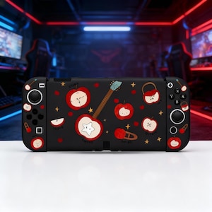 Puede incluir: Funda negra para Nintendo Switch con un estampado repetido de manzanas rojas, instrumentos musicales y estrellas. La funda tiene un acabado brillante y presenta las palabras "Clock", "Apple", "Guitar" y "Desire".