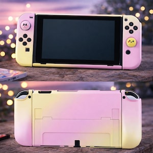 Puede incluir: Una consola Nintendo Switch con degradado rosa y amarillo y una pantalla negra. Los mandos presentan diseños de personajes de dibujos animados. La consola se muestra sobre una superficie de piedra, mostrando tanto la parte delantera como la trasera.