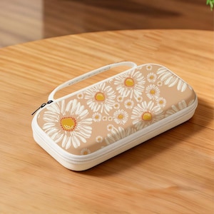 May include: A beige zippered case with a white handle and a daisy pattern. The case has a white zipper and a white handle. The daisy pattern has white petals and yellow centers. The case is on a wooden surface.