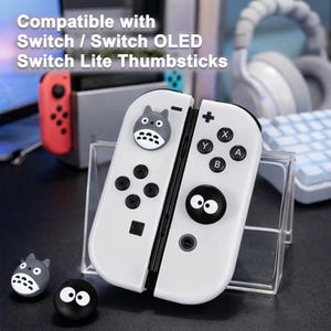 May include: White Nintendo Switch controllers with black buttons and a cartoon character design. The text "Compatible with Switch / Switch OLED Switch Lite Thumbsticks" is visible at the top of the image. Additional character thumbsticks are also present.