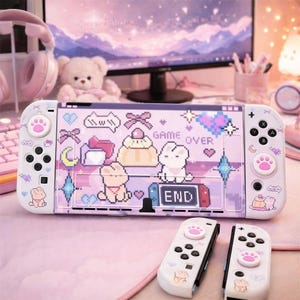 May include: A pink and white Nintendo Switch console with matching controllers. The console has a pixelated design with bunnies, hearts, and the words "GAME OVER" and "END". The controllers have paw print designs.