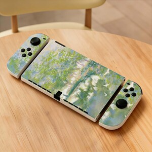 Könnte beinhalten: Eine Nintendo Switch-Konsole mit einem individuellen Skin, der eine Naturszene in Grün-, Blau- und Weißtönen zeigt. Die Joy-Con-Controller und das Konsolengehäuse haben ein passendes Design. Die Konsole liegt auf einer Holzoberfläche.