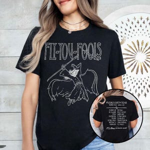 May include: Black t-shirt with the text "FLY YOU FOOLS" above a white illustration of a figure with a spear. The back of the shirt has a list of text that reads "MIDDLE-EARTH TOUR THIRD AGE 3018-3019".