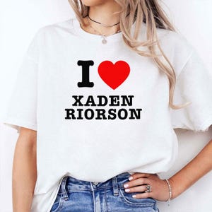 May include: White t-shirt with the text "I ♥ XADEN RIORSON" in black and red. The heart symbol is red. The shirt is a casual style.