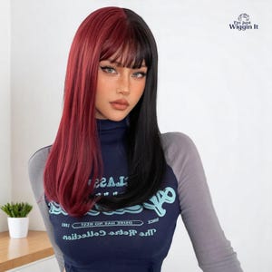 May include: A two-tone wig with a striking split design: one side is a deep red, the other black. The wig has a fringe and straight, shoulder-length hair. The wearer is wearing a navy blue and grey long-sleeved top.