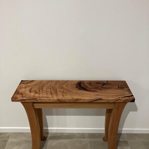 May include: A handcrafted wooden console table with a natural wood grain finish. The table has a rectangular top and four curved legs. The table is approximately 122 cm long, 41 cm wide, and 76 cm tall.