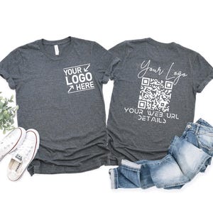 May include: Two grey t-shirts with white text and a QR code. One shirt has "YOUR LOGO HERE" printed on the front. The other shirt has "Your Logo" and a QR code with "YOUR WEB URL DETAILS" printed on the back. A pair of jeans and white trainers are in the image.