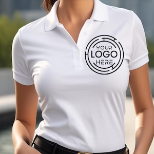 May include: White polo shirt with short sleeves and a collar. The shirt features a black circular logo that says "YOUR LOGO HERE". The shirt has a black belt and is made of a smooth, likely synthetic material.