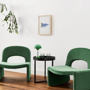 Peut inclure: Deux fauteuils en velours vert avec un dossier arrondi et une d&eacute;coupe. Une petite table d'appoint noire avec une lampe verte et deux verres se trouve entre les chaises. Une banni&egrave;re encadr&eacute;e avec le texte "TARHEELS" est accroch&eacute;e au mur blanc.