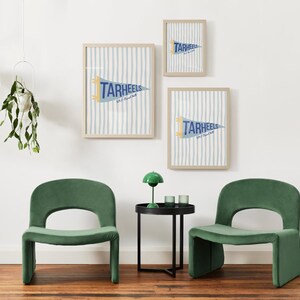 Peut inclure: Trois impressions encadr&eacute;es avec un fond &agrave; rayures bleues et blanches et un fanion qui se lit "TARHEELS". Deux chaises en velours vert et une petite table d'appoint noire avec une lampe verte et deux verres au premier plan.