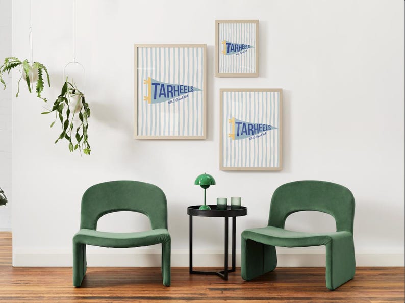 Peut inclure: Trois impressions encadr&eacute;es avec un fond &agrave; rayures bleues et blanches et un fanion qui se lit "TARHEELS". Deux chaises en velours vert et une petite table d'appoint noire avec une lampe verte et deux verres au premier plan.
