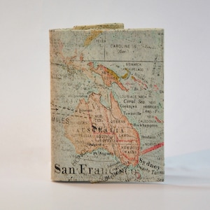 Könnte beinhalten: Eine Vintage-Karte von Australien mit einer abgenutzten, strukturierten Papieroberfläche. Die Karte zeigt die wichtigsten Städte und geografischen Merkmale des Landes, darunter das Korallenmeer, Neuguinea und die Salomonen. Die Karte ist in Braun-, Grün- und Rottönen gedruckt.