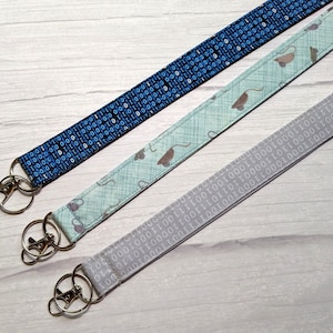 May include: Three keychains with different patterns. The first keychain is blue with a white binary code pattern. The second keychain is light blue with a white and grey pattern of mice. The third keychain is grey with a white binary code pattern.
