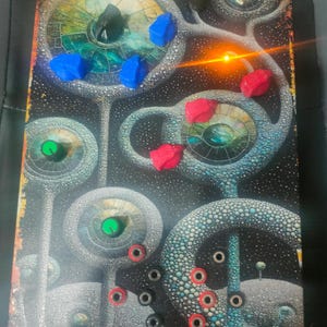 May include: A rectangular electronic synthesiser module featuring a dark, cosmic-themed graphic with circular, cell-like patterns. The interface includes multiple colourful knobs in blue, red, green, and yellow, along with several small circular input jacks.