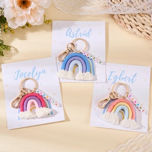 May include: Three rainbow keychains with personalized names on cards. Each keychain features a colorful rainbow design with a tassel base and a gold-colored clasp. The names "Astrid", "Jocelyn", and "Egbert" are spelled out with letter beads.