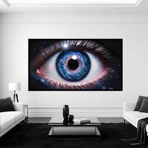 May include: A large framed art print featuring a close-up of a human eye with a cosmic galaxy design. The iris is a vibrant blue with a pink and purple center, surrounded by a black frame. The artwork is displayed in a modern living room setting.