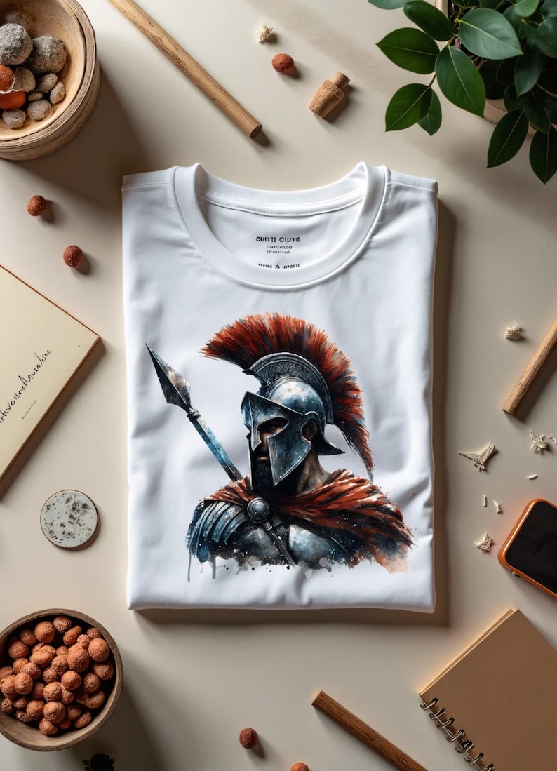 May include: White t-shirt featuring a watercolor illustration of a Spartan warrior with a spear. The warrior is depicted in a helmet and armor with a red plume. The shirt has the text "OUTIE CLUYE" on the tag.