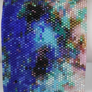 May include: A beaded bracelet with a blue, turquoise, pink, and black abstract pattern.